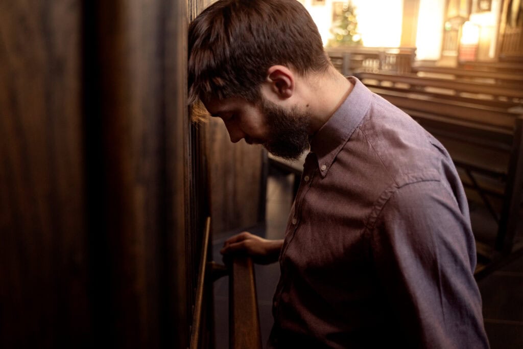 a man in am empty church with his head on the wall symbolizing exhaustion from religious striving
