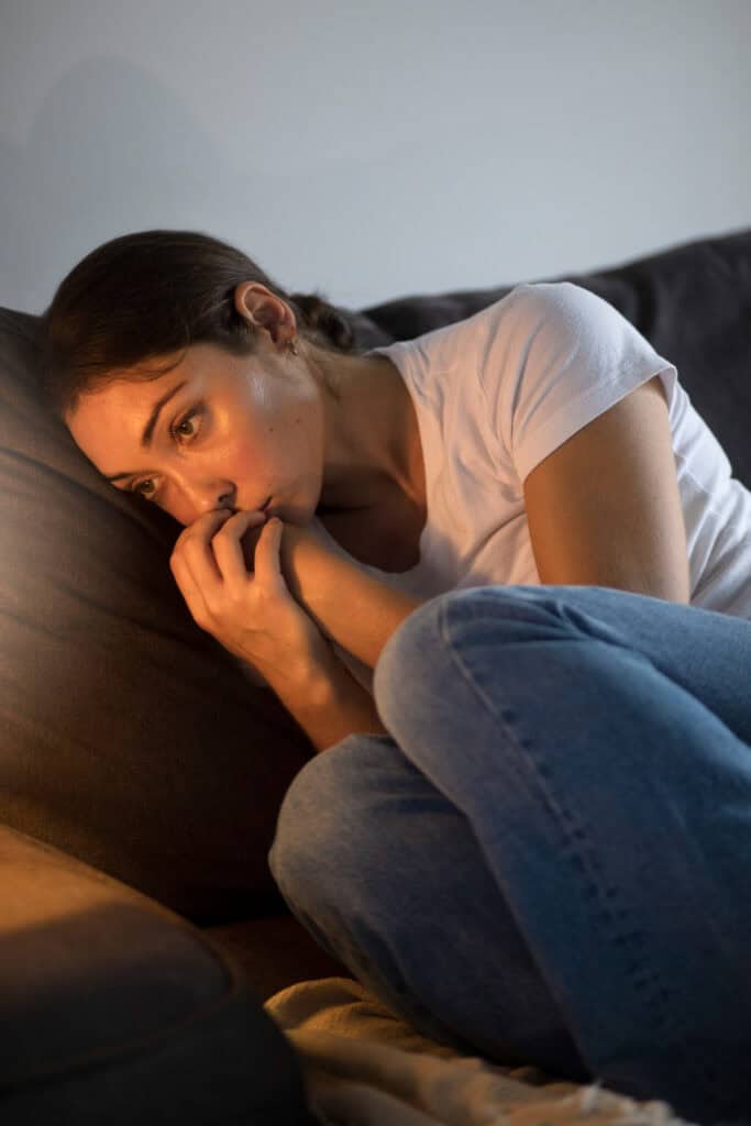 a young woman cuddled on the couch staring into the distance feeling alone and disconnected