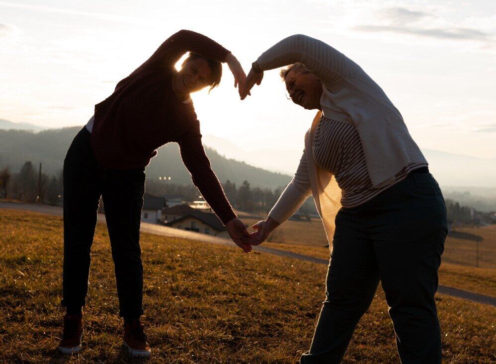 two people outside in the setting sun forming a heart with their hands