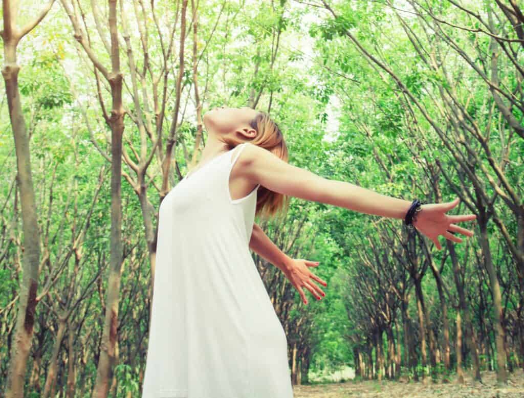 A woman with her arms wide open in a forrest symbolizing spiritual connection and letting go of striving
