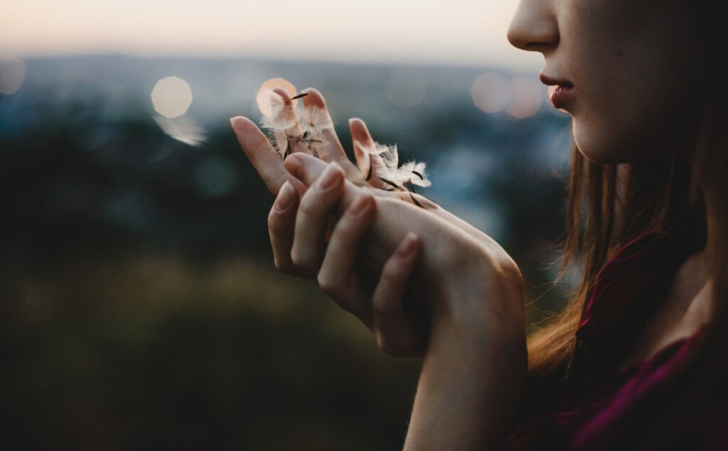 a woman blowing away dandelion pedals symbolizing restful letting go
