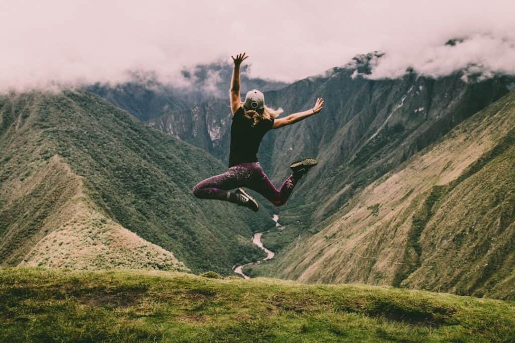 a woman jumping in joy on a green mountain