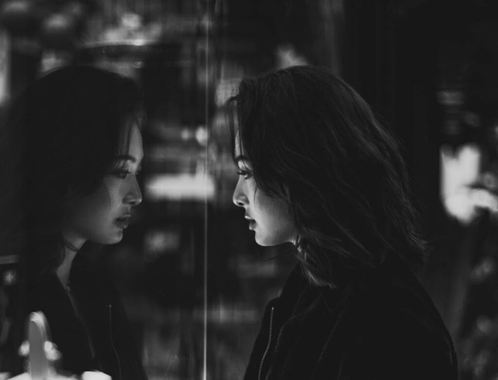 a black and white image of a woman looking into her reflection in a store window symbolizing her sense of identity