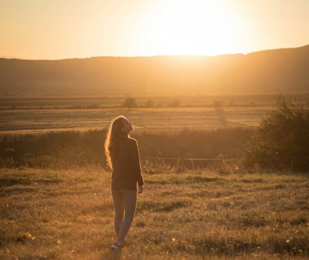 a woman walking in a field with the sun shining symbolizing a daily walk with the putting love in action so she is experiencing God on a deeper level.