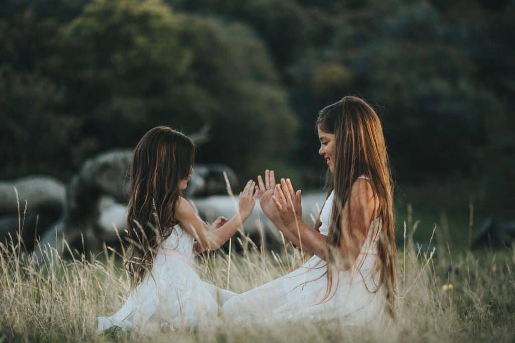two girls playing smiling in white dresses kneeling in the grass outside symbolizing the freedom and innocence of childhood prior to any trauma taking place