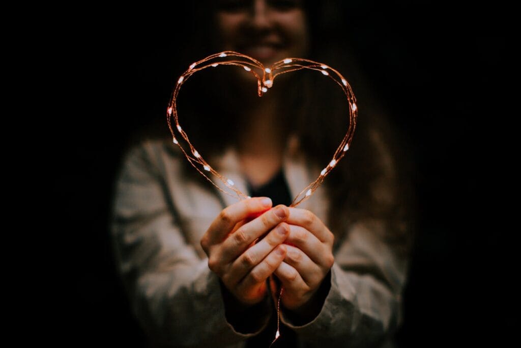 a woman smiling holding a heart made of lights symbolizing that she feels loved
