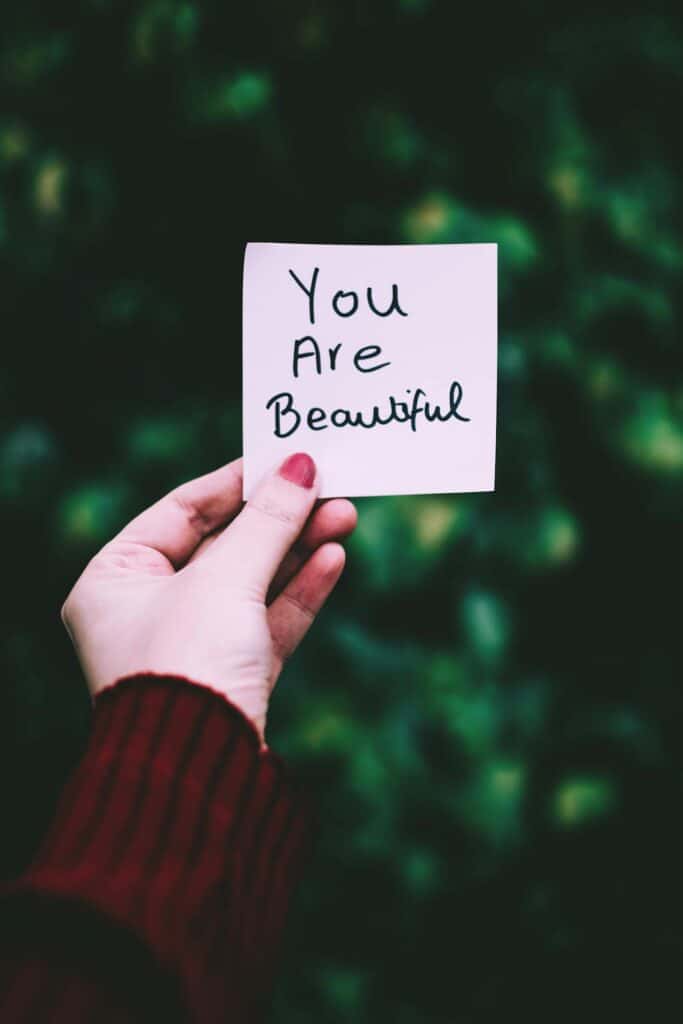 a woman's hand holding a note that says "You Are Beautiful" symbolizing the power of putting love in action through words